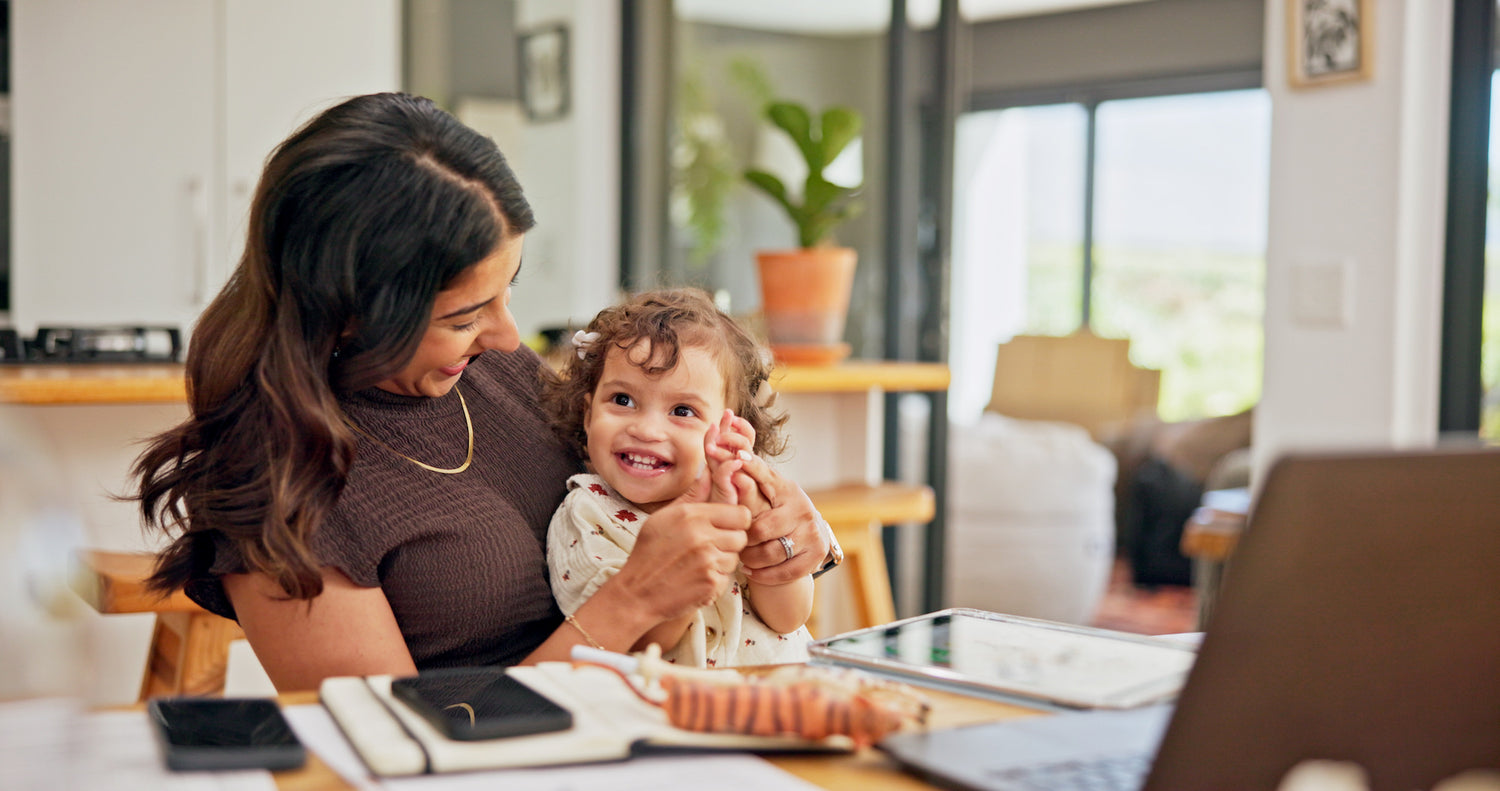 Woman and child sitting at a table with a laptop and phone, smiling.